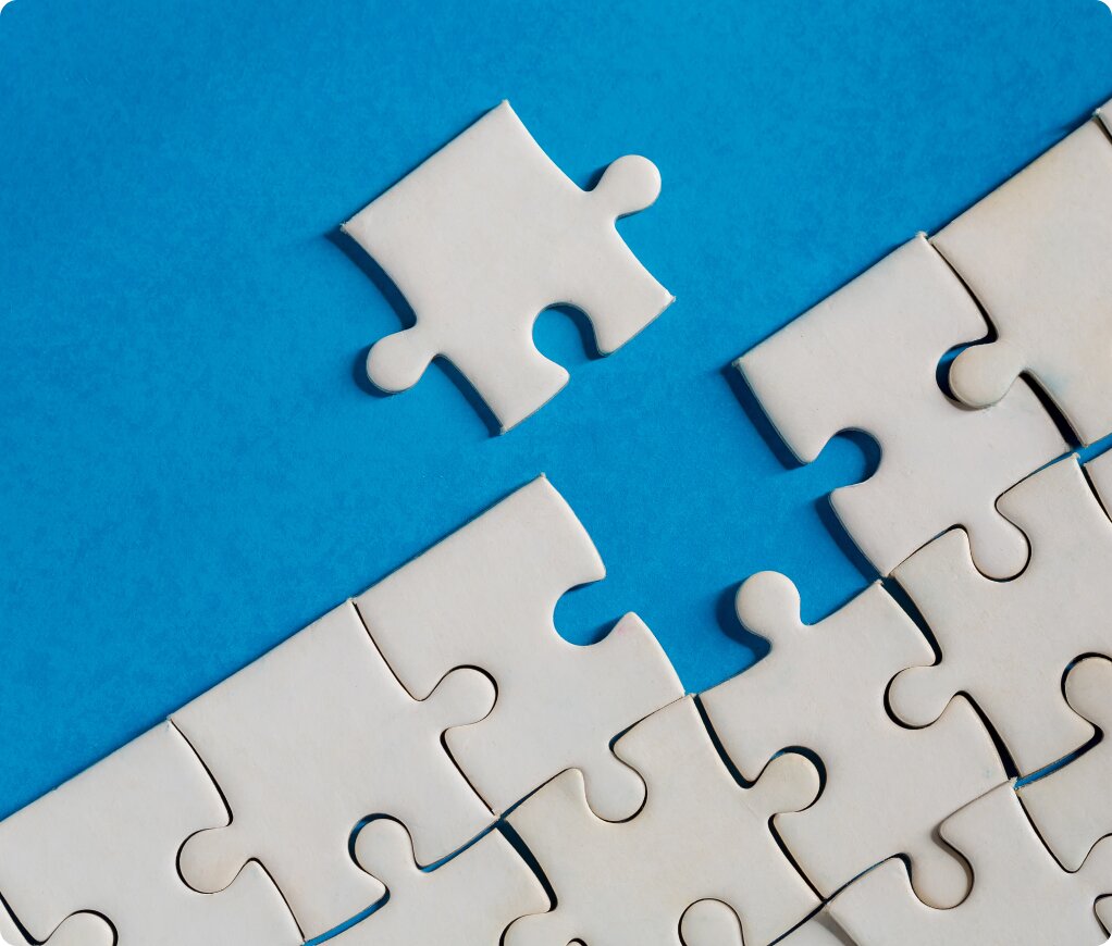 Single white puzzle piece about to complete a nearly finished puzzle over a bright blue background.